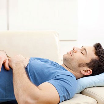 A man rests his back by laying down on the couch.