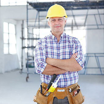 A male construction worker stands on site with his arms crossed.