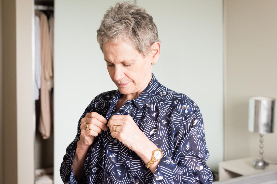 Senior or mature woman buttoning up shirt while getting dressed.