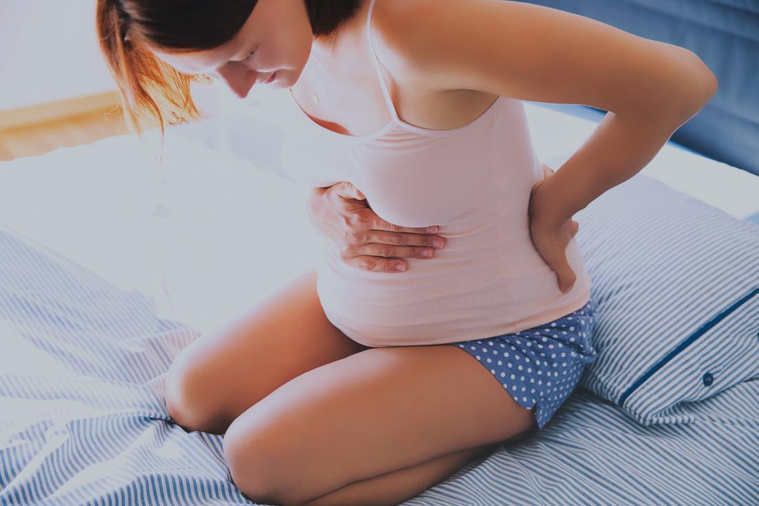 Pregnant woman sitting on bed looking down at bump experiencing blood show.