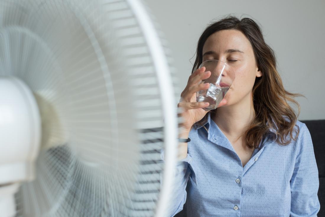 young woman sipping water in front of a fan
