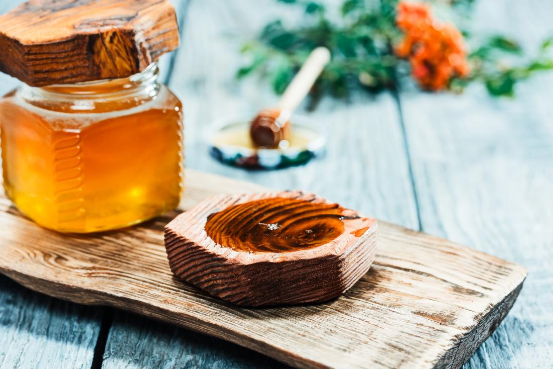 Honey on wooden board with honey jar and spoon.