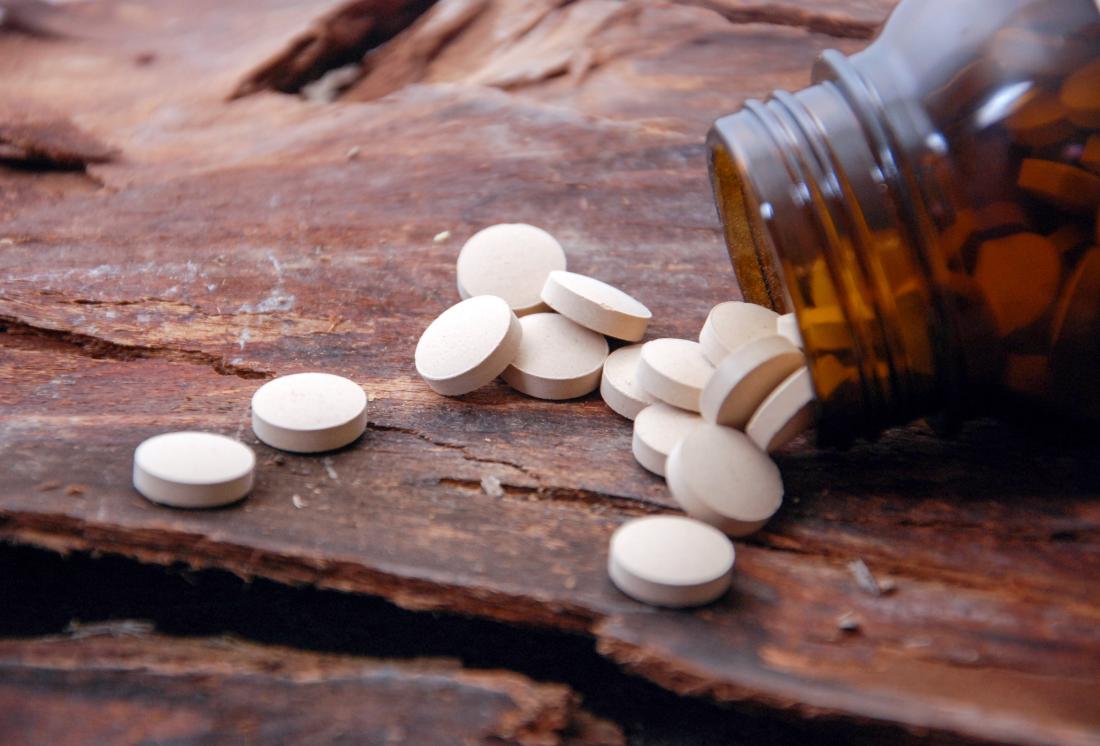 Vitamins and minerals supplements or pills spilling out of bottle onto wooden surface