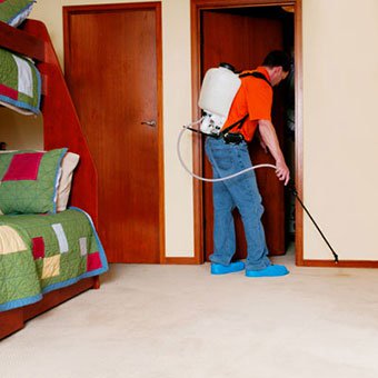 An exterminator sprays a bedroom for bedbugs.