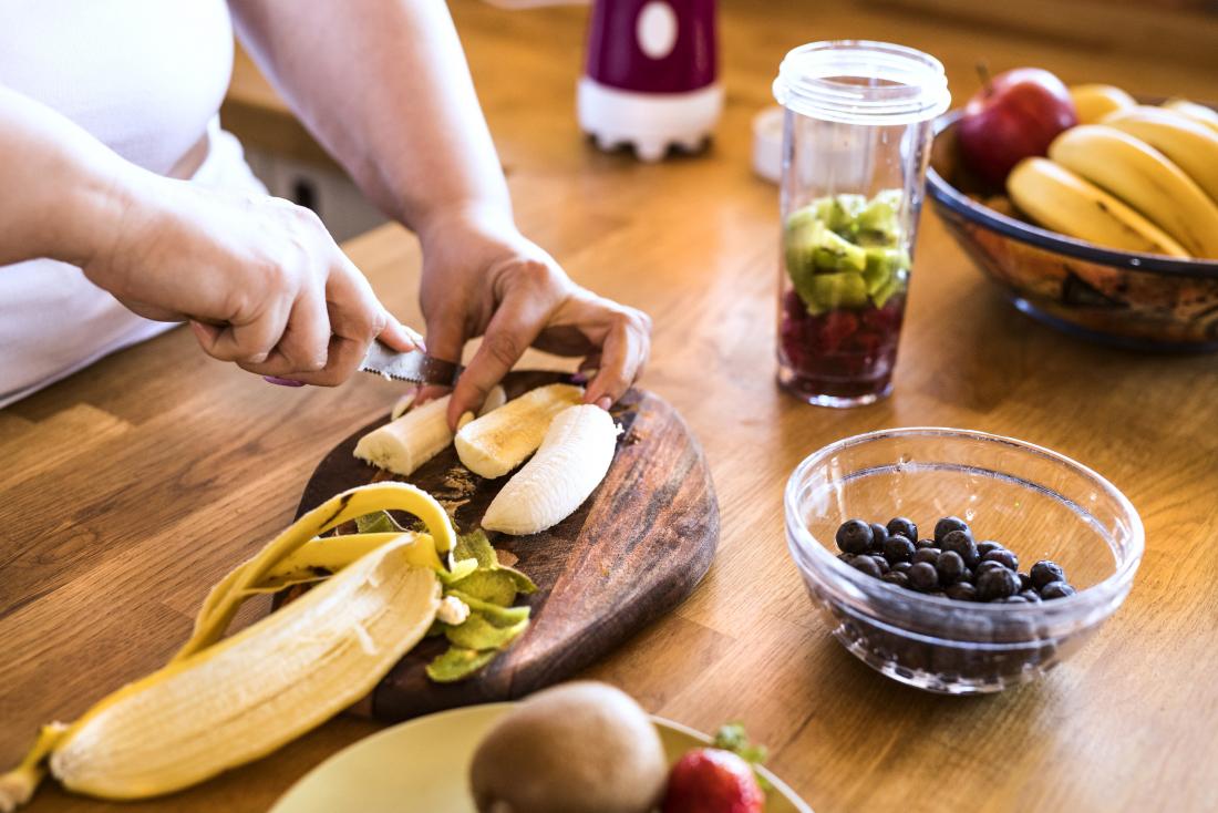 Person chopping or cutting fruits for smoothie or juice, including banana, kiwi, and blueberries