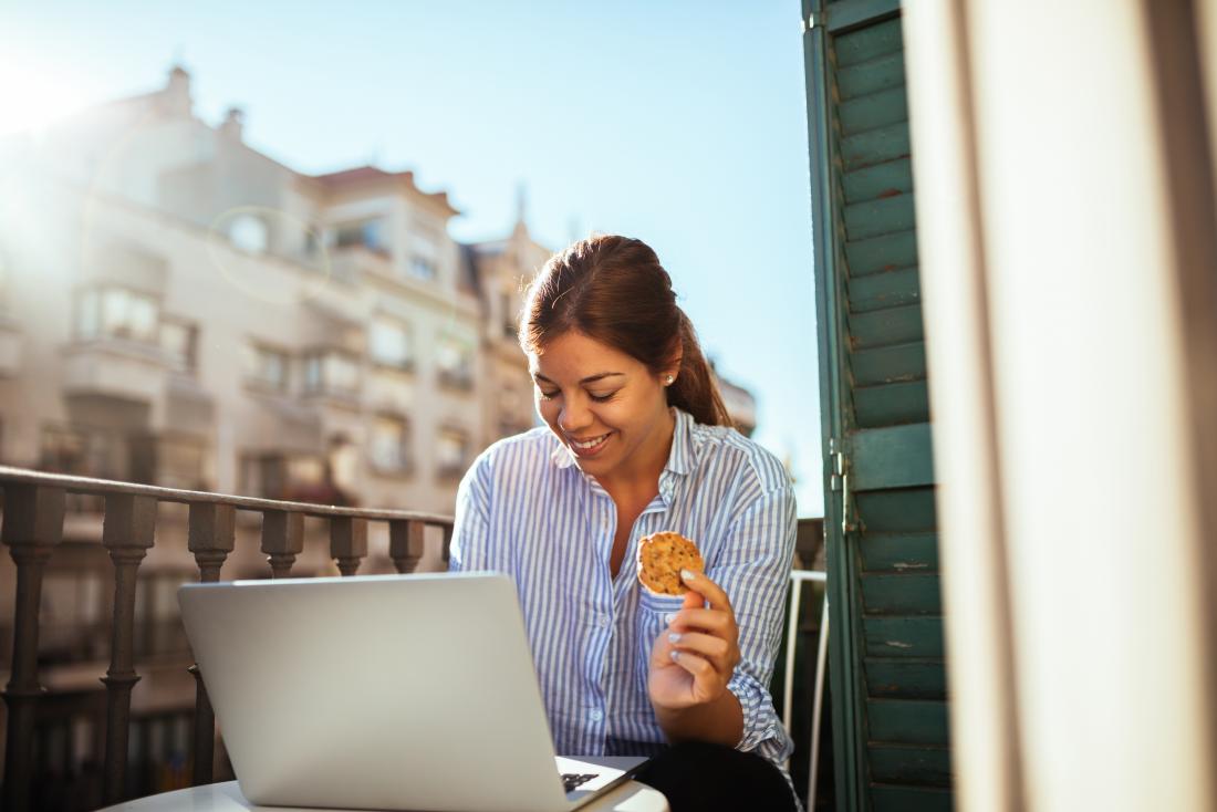young woman on laptop eating a cookie