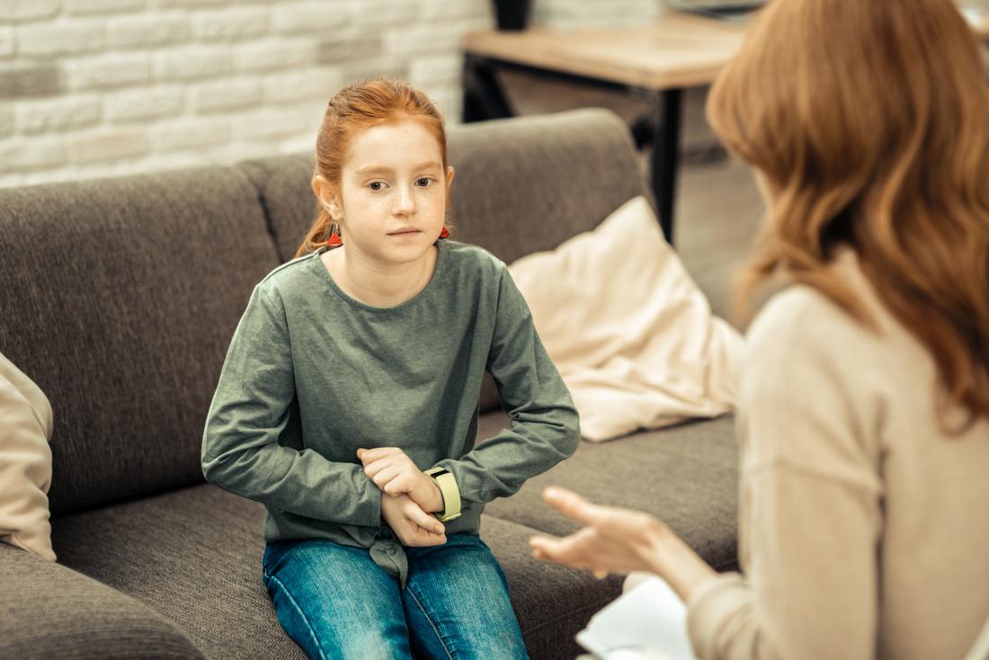 Child with autism in therapy speaking with adult or parent, avoiding eye contact and looking anxious