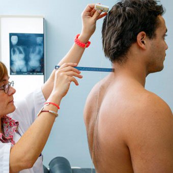 A doctor performs a clinical exam and looks for signs of scoliosis in an adult male.