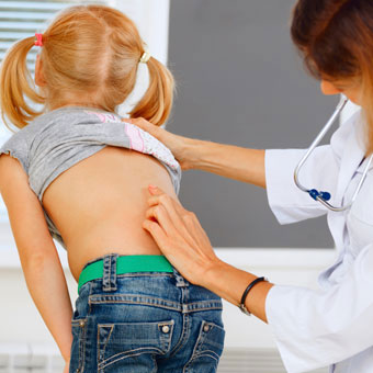 A doctor performs a scoliosis screening on a girl at school.
