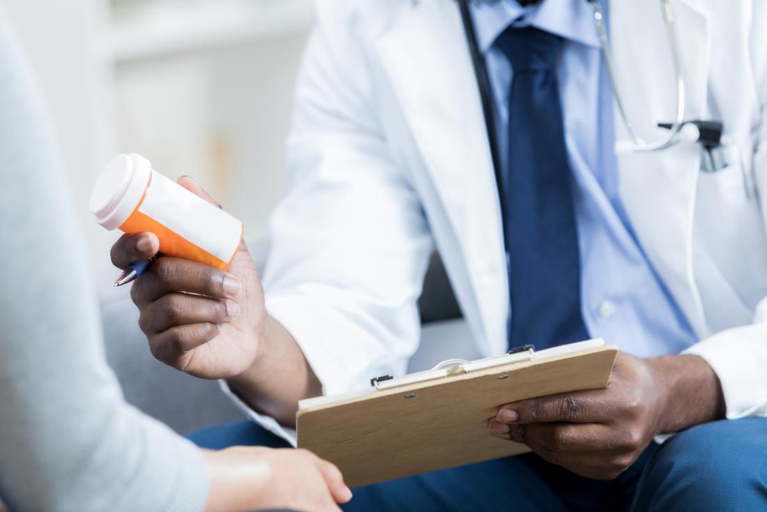 Doctor holding prescription medication bottle and showing it with clipboard to patient.