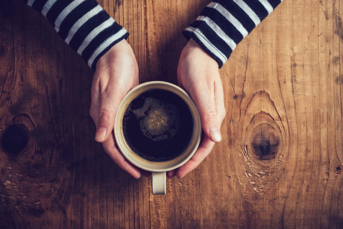 close up of a person's hands holding a cup of coffee against a wooden background