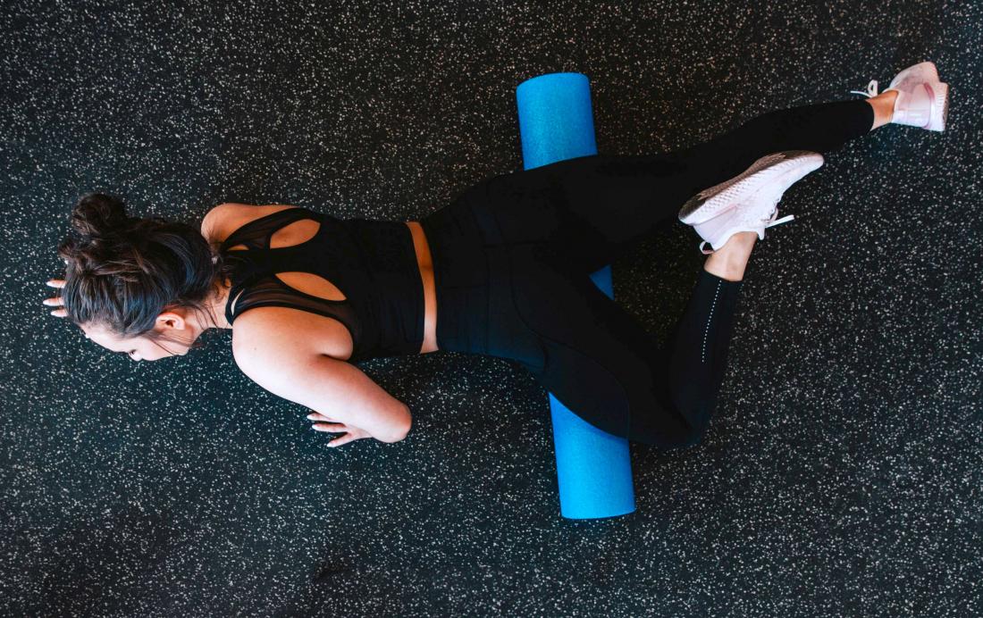 Woman using foam roller for stretching and muscle tension.