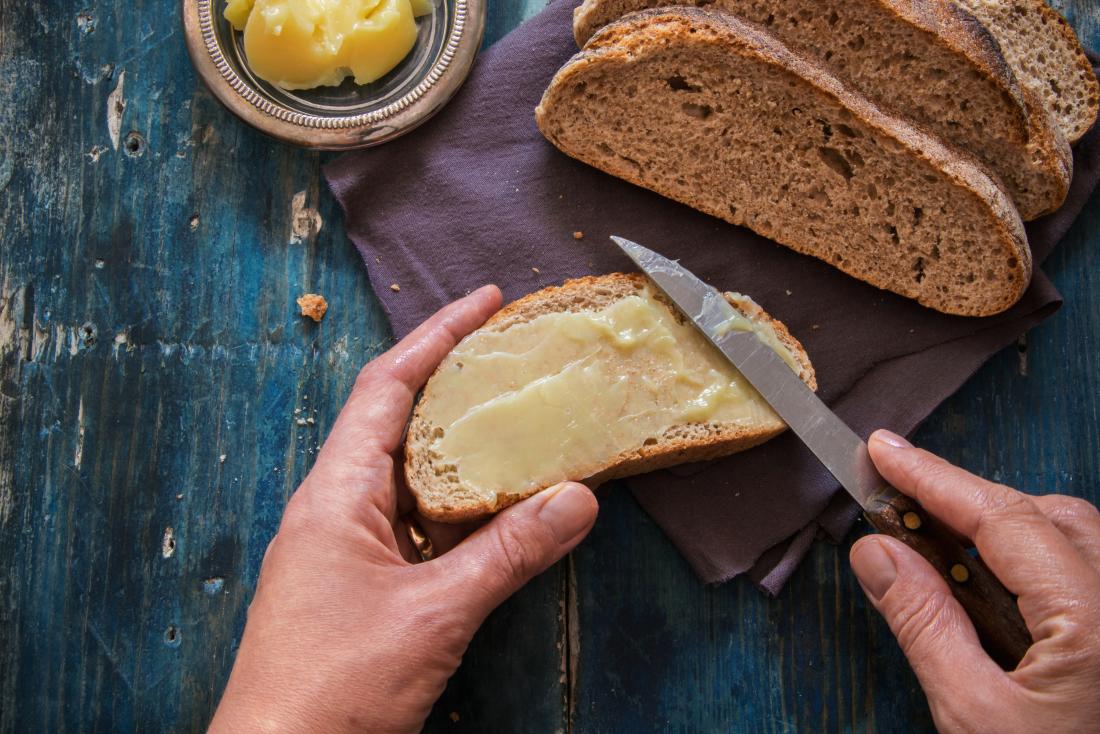 Person spreading grass fed butter onto whole grain bread