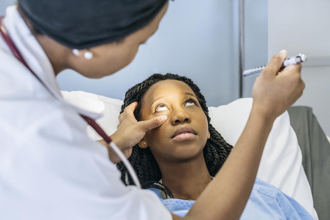 Doctor looking at womans eye to determine why pupils are different sizes