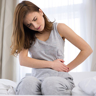 A woman sitting on her bed with lower left abdominal pain and tenderness.
