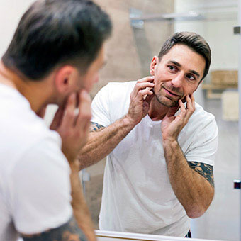 A man examines his face in the mirror.