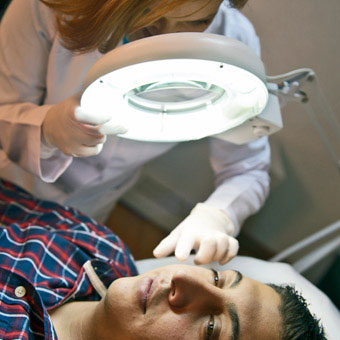 A dermatologist examines the face of a patient.
