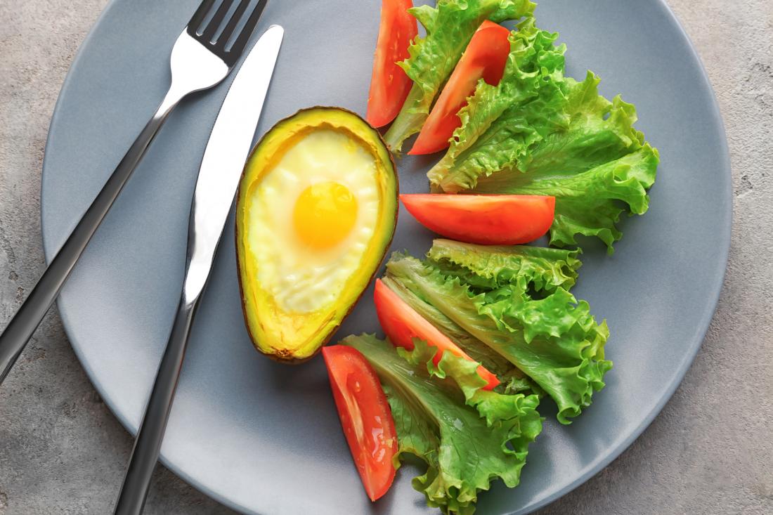 salad on a plate next to an egg in an avocado