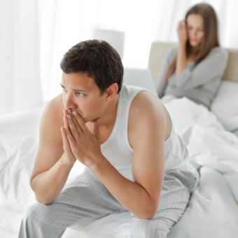 A worried man sits on the edge of the bed with his wife.