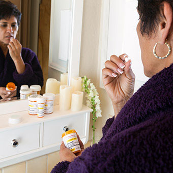 A womanin a bathroom taking pills.