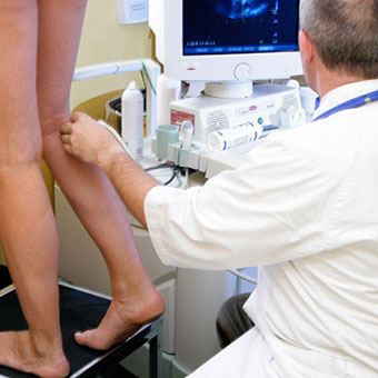 A doctor performs an ultrasound on the leg of a woman.