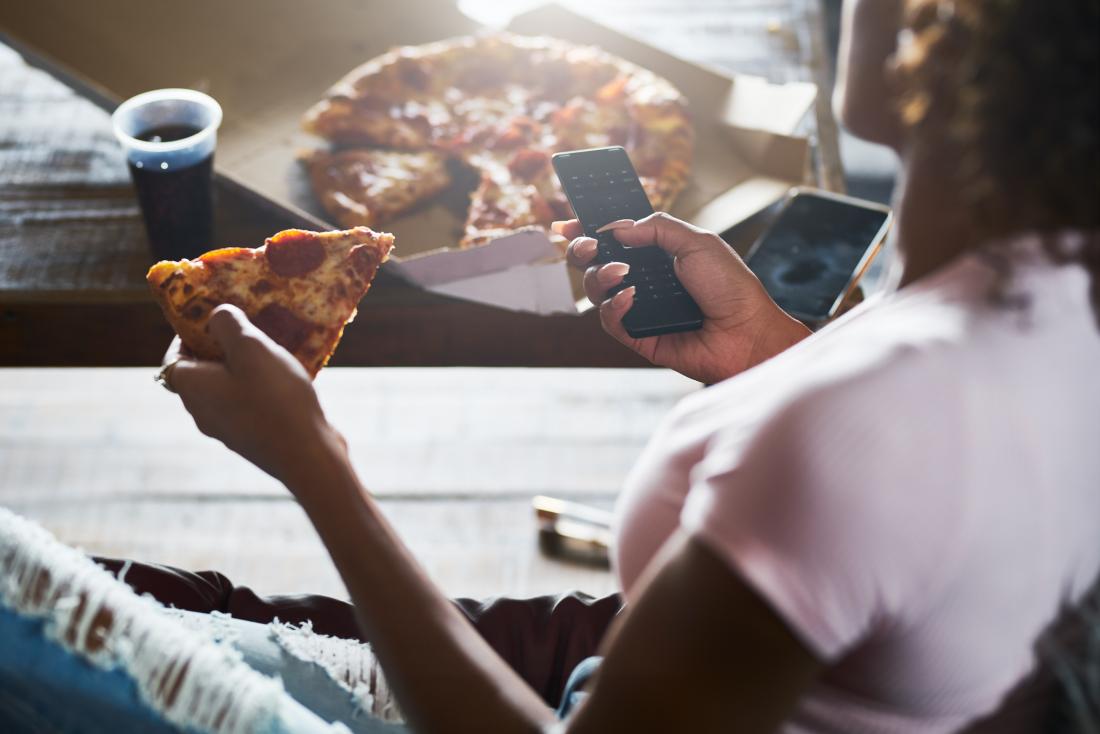 woman eating pizza while checking her phone