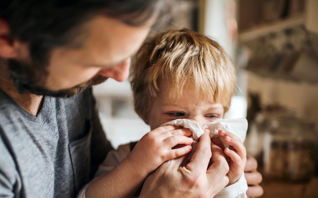 a dad blowing the nose of his toddler who is showing symptoms of the flu. 