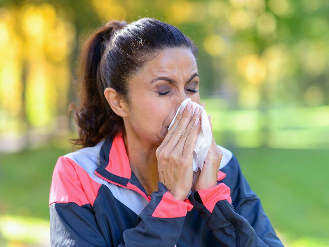 a woman blowing her nose as she is Working out while sick