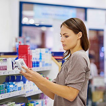 A woman reading the label of over-the-counter wart medication at the drug store.