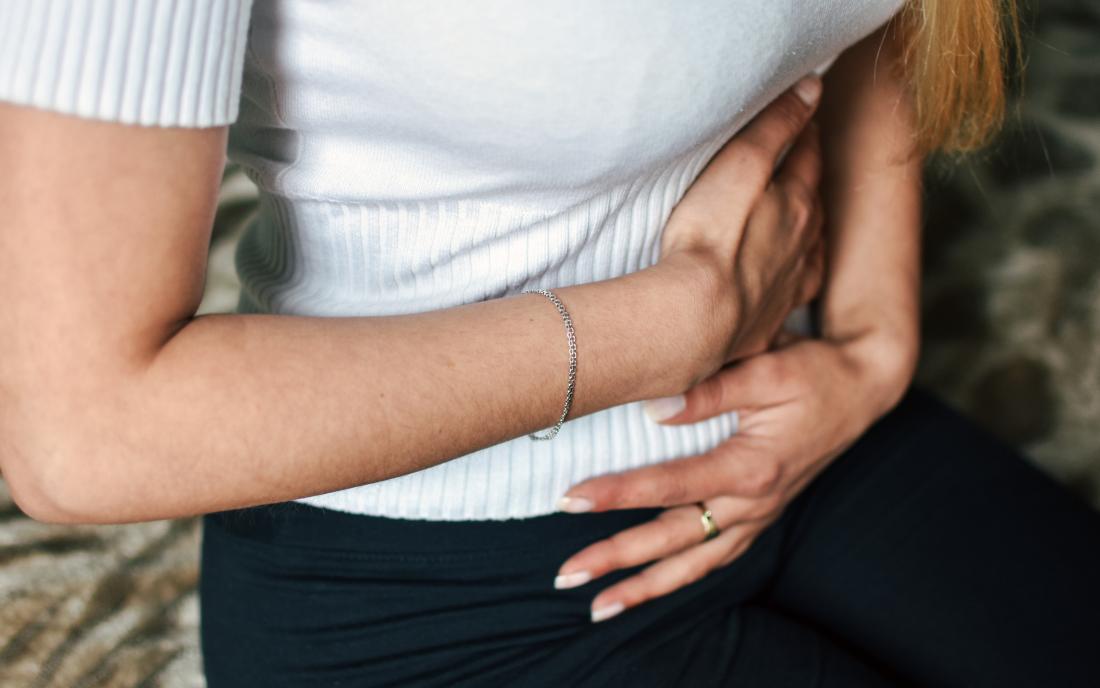 a woman holding her stomach as she is experiencing colon pain. 