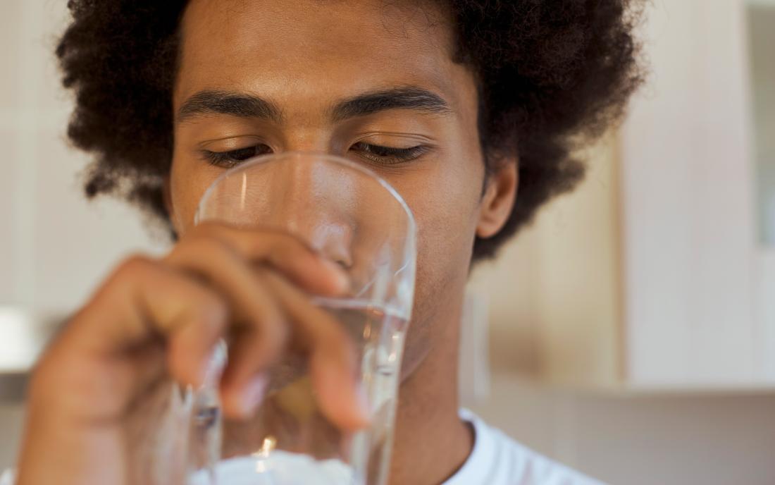 a man drinking a glass of water as it's one of many dry mouth remedies
