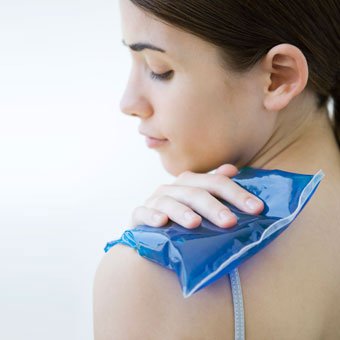 A woman places an ice compress on her shoulder.
