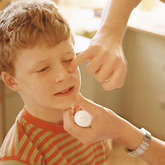 A father puts ointment on a boy's face.