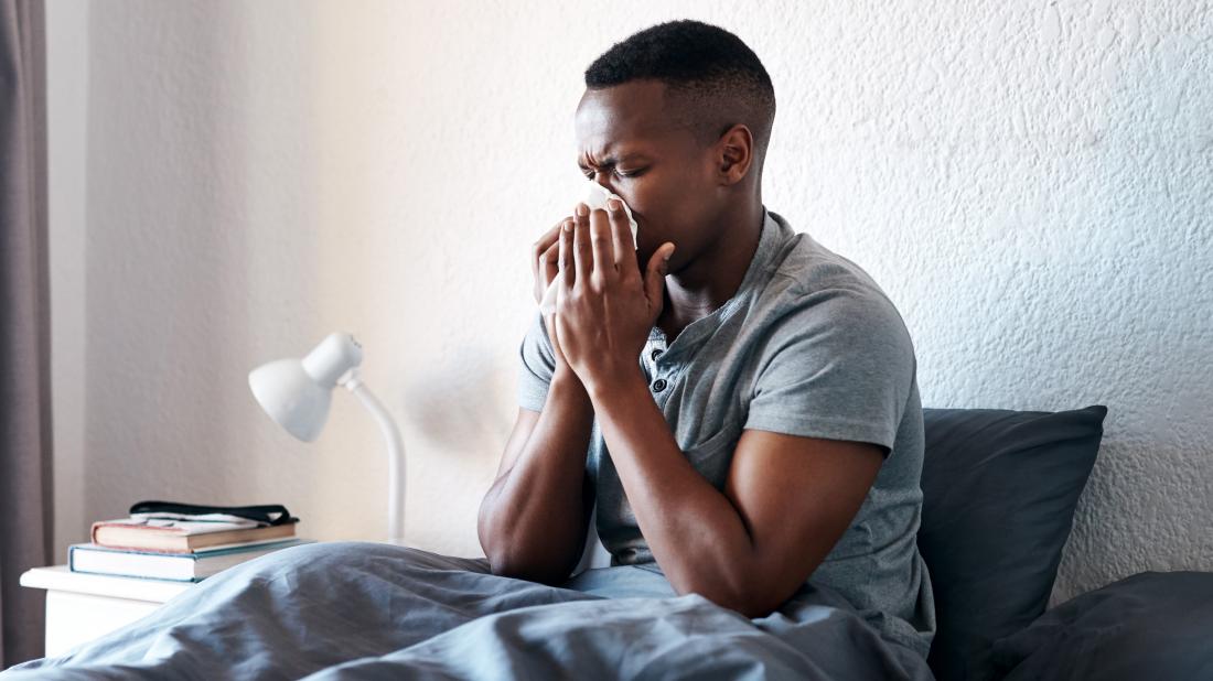 a man blowing his nose in bed because he has either influenza a or b